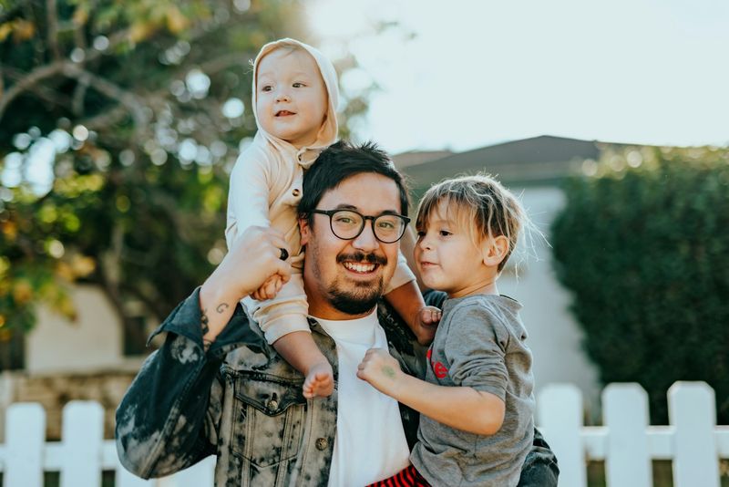 Pai com dois filhos pequenos em frente de casa