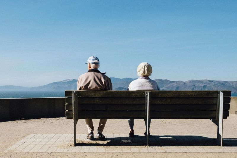 Casal de idosos sentado em banco de frente para o mar